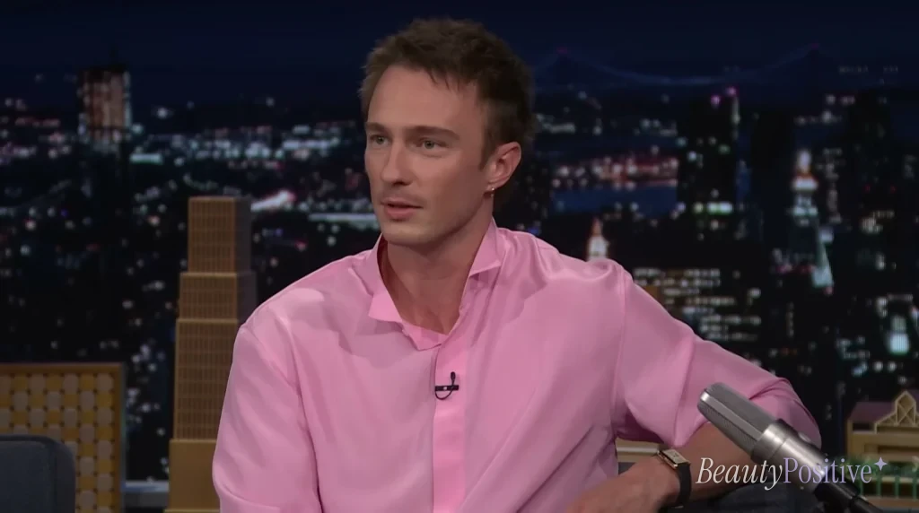 Drew Starkey in a pink shirt talking on the couch of The Tonight Show Starring Jimmy Fallon