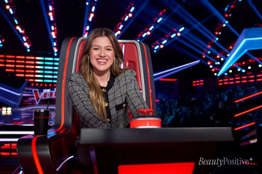 Kelly Clarkson smiling in her coach's chair on the set of The Voice